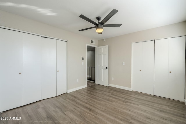 unfurnished bedroom featuring ceiling fan, light wood-type flooring, and two closets