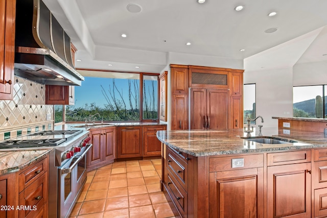 kitchen featuring premium appliances, light tile floors, wall chimney range hood, tasteful backsplash, and sink