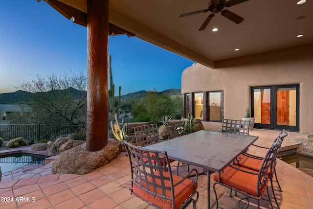 patio terrace at dusk with a fenced in pool, a mountain view, ceiling fan, and french doors