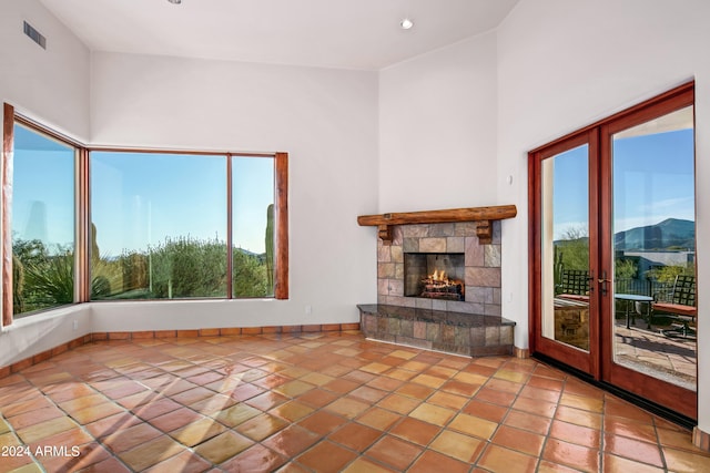 unfurnished living room featuring a stone fireplace, light tile floors, high vaulted ceiling, and french doors