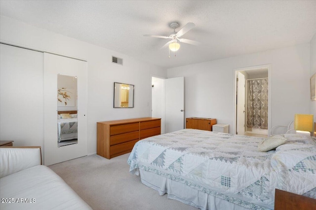 bedroom with ensuite bathroom, ceiling fan, a textured ceiling, light colored carpet, and a closet