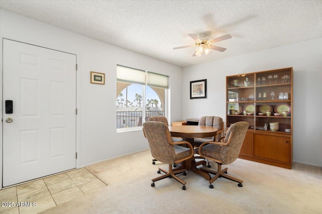 dining space with ceiling fan, light colored carpet, and a textured ceiling