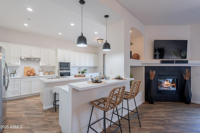 kitchen featuring stainless steel appliances, dark wood-type flooring, light countertops, recessed lighting, and an island with sink