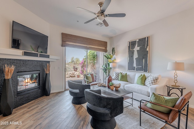 living room with wood finished floors, ceiling fan, a glass covered fireplace, and baseboards