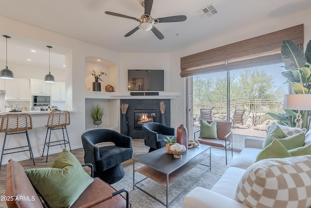 living area with ceiling fan, a glass covered fireplace, wood finished floors, and recessed lighting