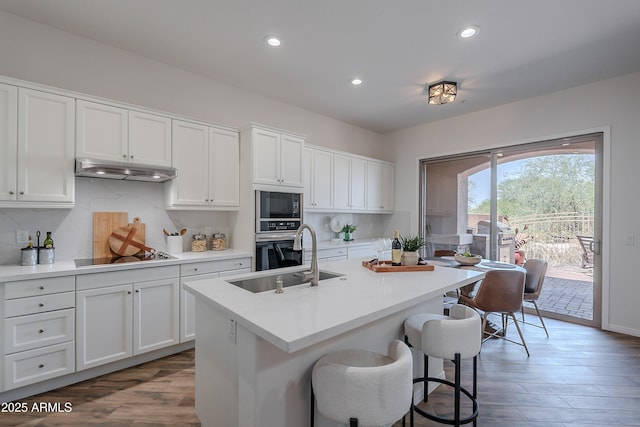 kitchen featuring a sink, black appliances, under cabinet range hood, decorative backsplash, and recessed lighting
