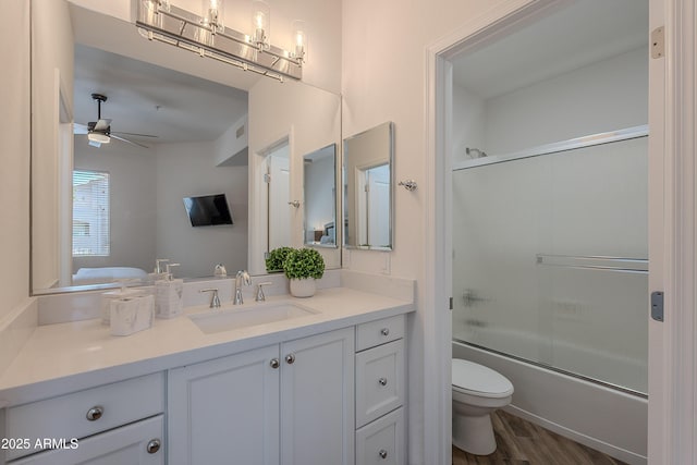 full bath featuring toilet, vanity, ceiling fan, bath / shower combo with glass door, and wood finished floors
