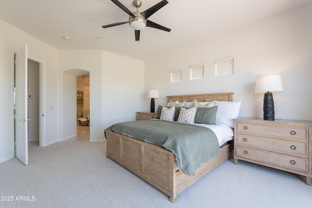 bedroom featuring arched walkways, light carpet, baseboards, connected bathroom, and a ceiling fan