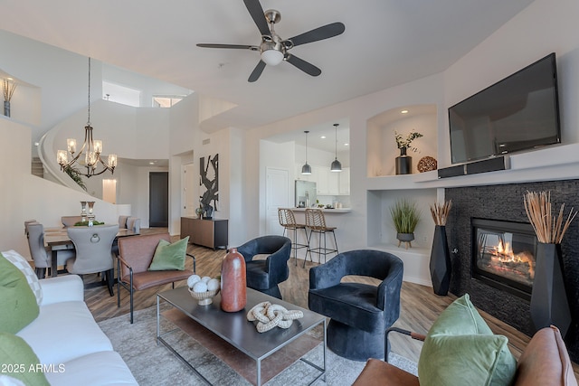 living area with light wood-style flooring, a ceiling fan, a glass covered fireplace, and a chandelier