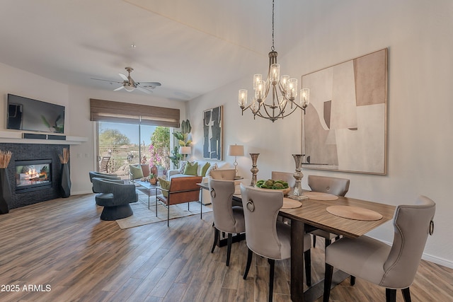 dining space with wood finished floors, a chandelier, a glass covered fireplace, baseboards, and ceiling fan