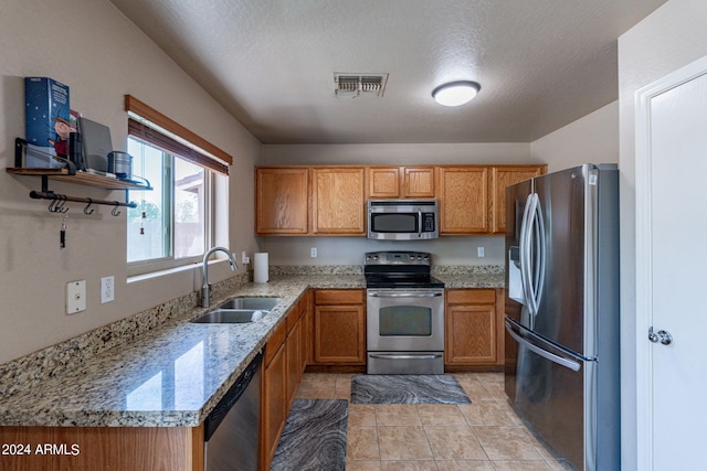 kitchen featuring light stone counters, light tile patterned floors, stainless steel appliances, a textured ceiling, and sink