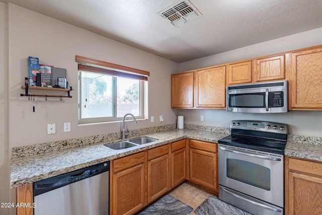 kitchen featuring light tile patterned floors, sink, a textured ceiling, appliances with stainless steel finishes, and light stone countertops