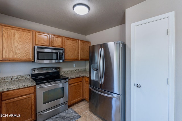 kitchen with a textured ceiling, light tile patterned flooring, stainless steel appliances, and light stone counters