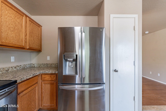 kitchen with a textured ceiling, light stone counters, light hardwood / wood-style floors, and stainless steel fridge