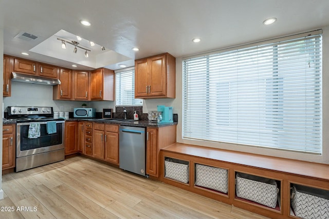 kitchen featuring dark stone counters, sink, light hardwood / wood-style floors, and appliances with stainless steel finishes