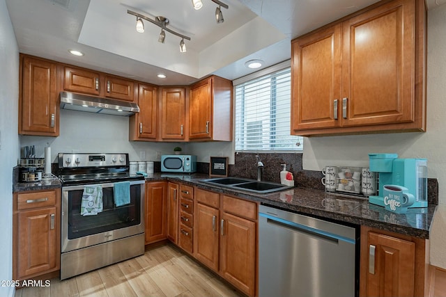 kitchen featuring appliances with stainless steel finishes, rail lighting, sink, light hardwood / wood-style flooring, and dark stone countertops