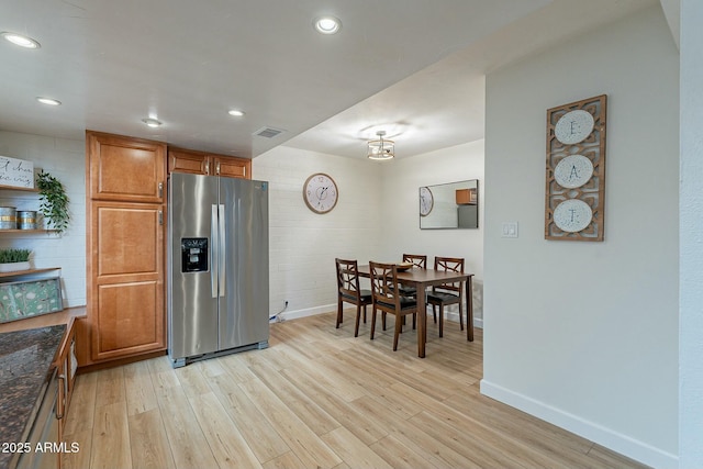 kitchen with dark stone countertops, stainless steel fridge, brick wall, and light wood-type flooring