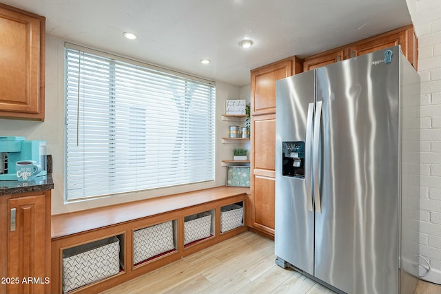 kitchen with stainless steel fridge, light wood-type flooring, and dark stone counters