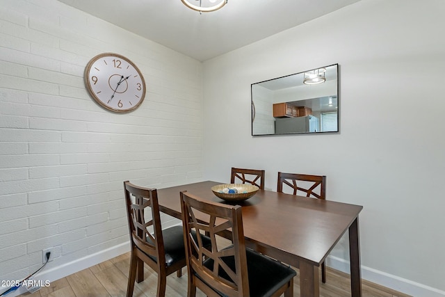 dining room featuring light wood-type flooring and brick wall