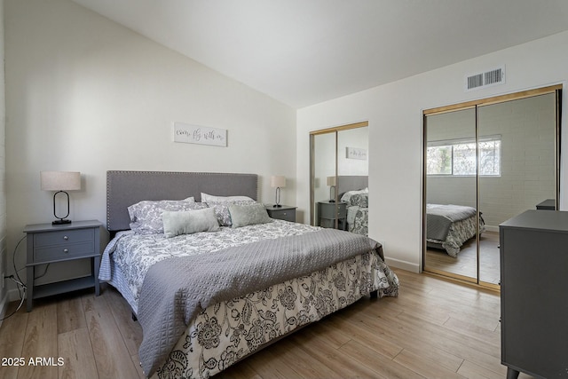 bedroom featuring light wood-type flooring, vaulted ceiling, and multiple closets