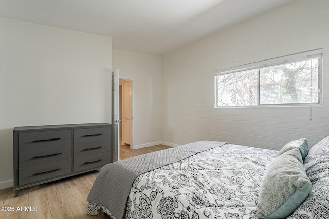 bedroom with light wood-type flooring and brick wall