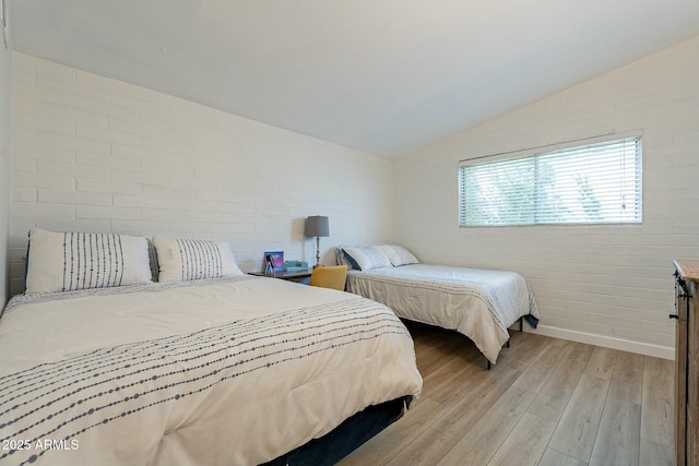 bedroom with brick wall, lofted ceiling, and light hardwood / wood-style floors