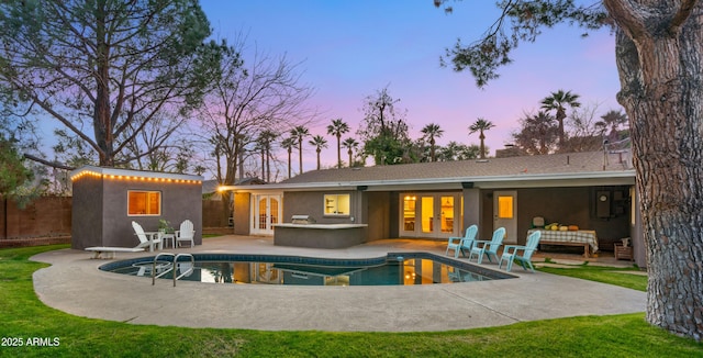 back house at dusk featuring an outbuilding, french doors, and a patio