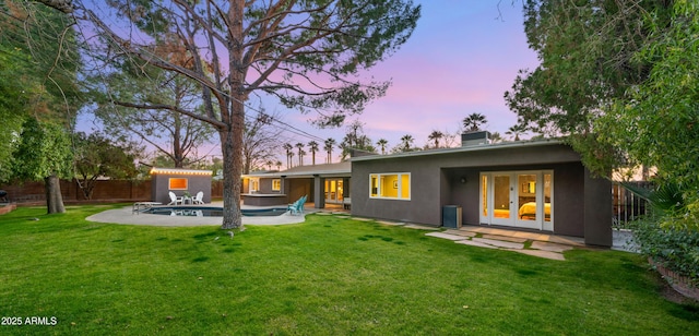 back house at dusk with a patio area, a fenced in pool, a lawn, and french doors