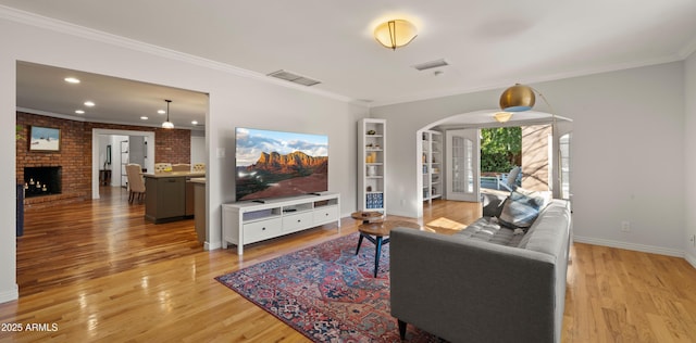 living room with a fireplace, ornamental molding, and light wood-type flooring