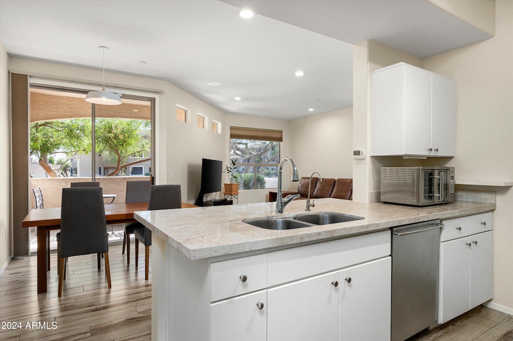 kitchen featuring light wood-type flooring, hanging light fixtures, white cabinetry, and sink