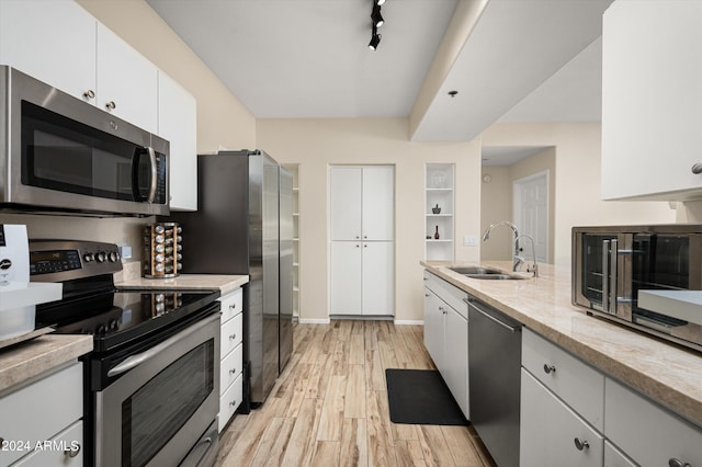 kitchen with light wood-type flooring, light stone counters, sink, white cabinetry, and stainless steel appliances