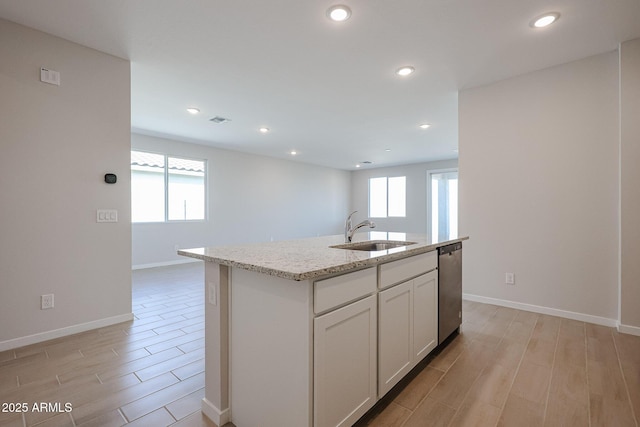 kitchen featuring sink, white cabinetry, light stone counters, dishwasher, and an island with sink