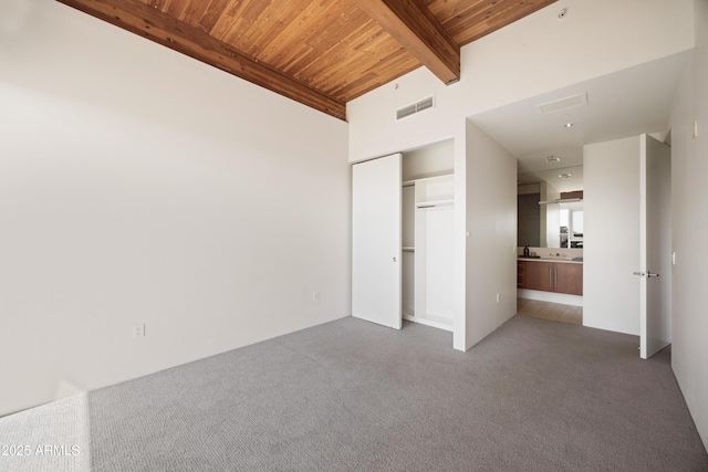 unfurnished bedroom with visible vents, beam ceiling, a closet, carpet floors, and wooden ceiling