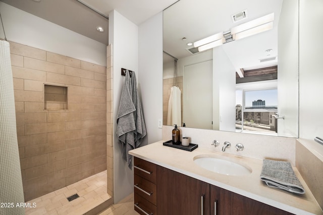 full bath with a tile shower, visible vents, and vanity