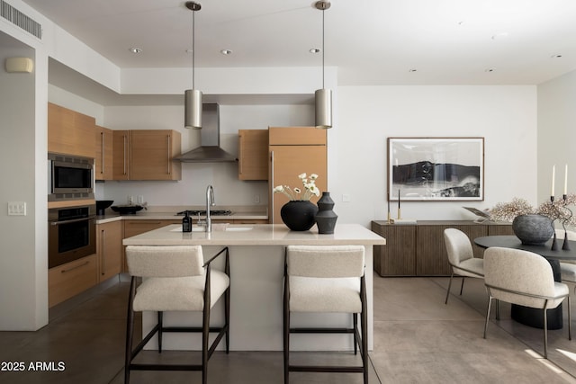 kitchen featuring visible vents, stainless steel appliances, light countertops, wall chimney range hood, and brown cabinets