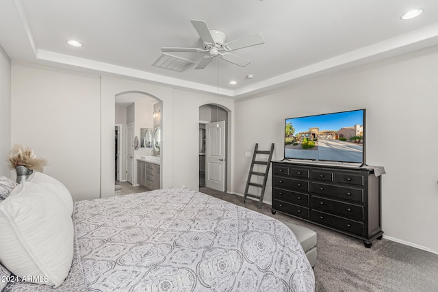 carpeted bedroom featuring ensuite bathroom, ceiling fan, and a tray ceiling