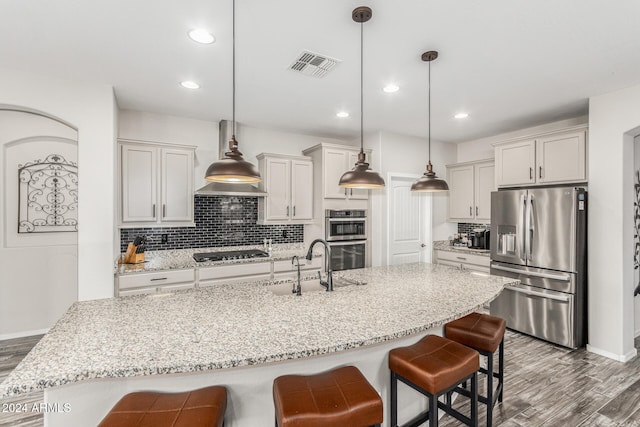 kitchen with stainless steel appliances, light stone countertops, light wood-type flooring, pendant lighting, and decorative backsplash