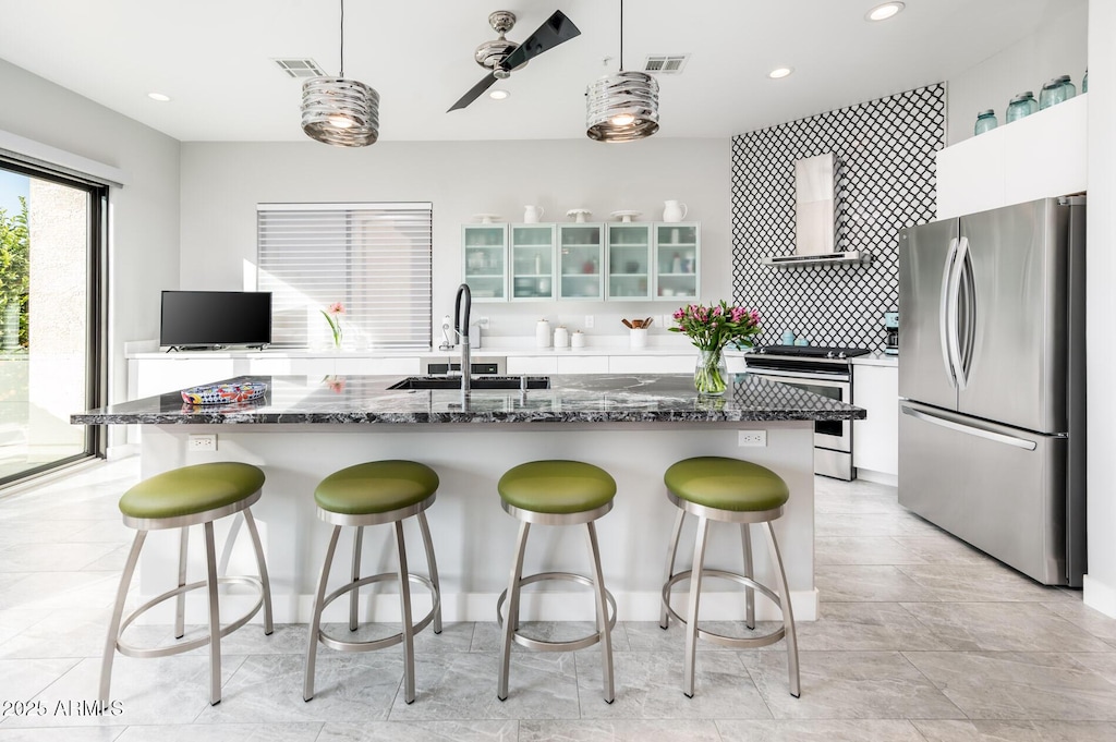 kitchen with white cabinets, appliances with stainless steel finishes, pendant lighting, and wall chimney range hood