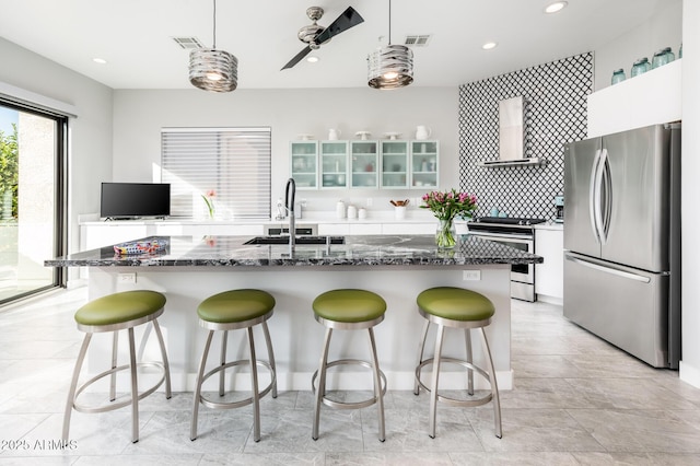 kitchen with white cabinets, appliances with stainless steel finishes, pendant lighting, and wall chimney range hood