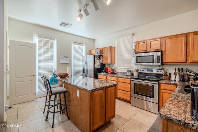 kitchen featuring appliances with stainless steel finishes, light tile patterned floors, stone counters, a breakfast bar area, and a center island