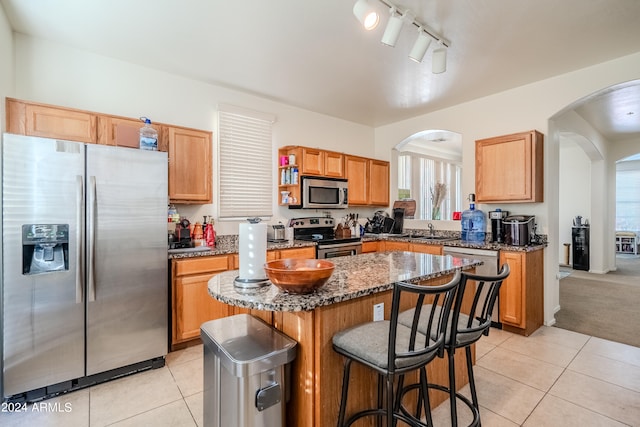 kitchen featuring sink, appliances with stainless steel finishes, dark stone counters, light tile patterned floors, and a center island