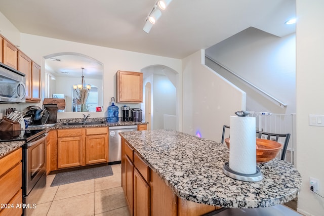 kitchen featuring stainless steel appliances, stone countertops, sink, light tile patterned floors, and an inviting chandelier