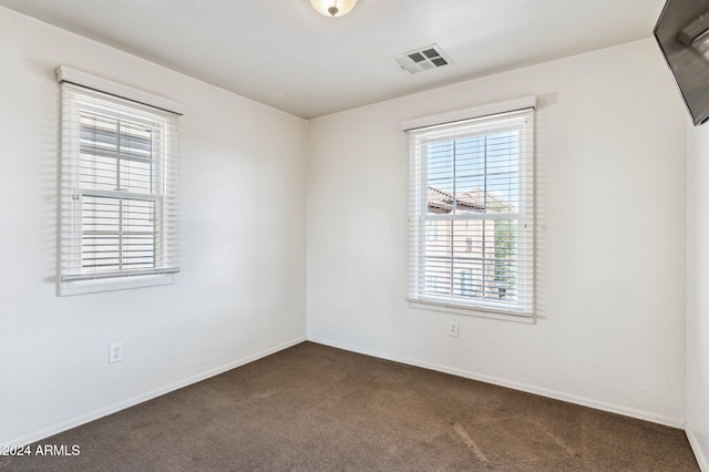 spare room featuring dark colored carpet and a wealth of natural light