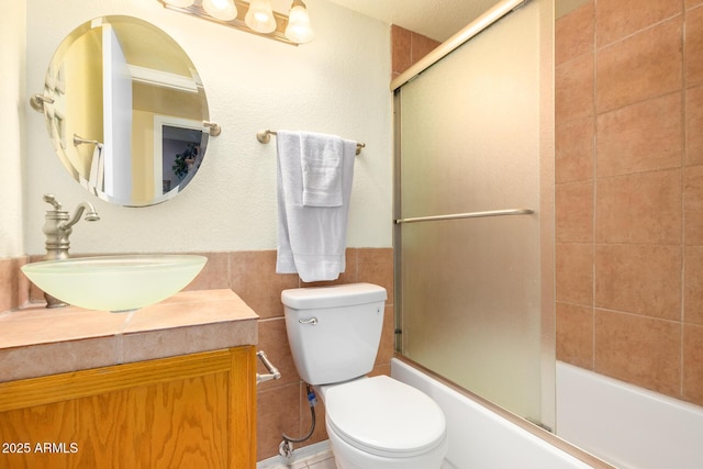 full bathroom with tile walls, vanity, combined bath / shower with glass door, and toilet