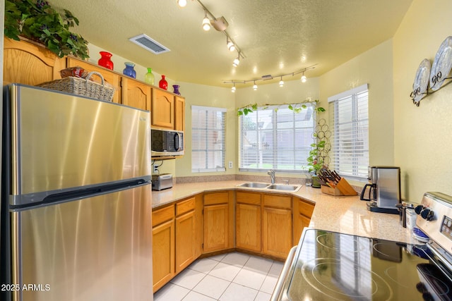 kitchen with appliances with stainless steel finishes, sink, light tile patterned floors, and a textured ceiling