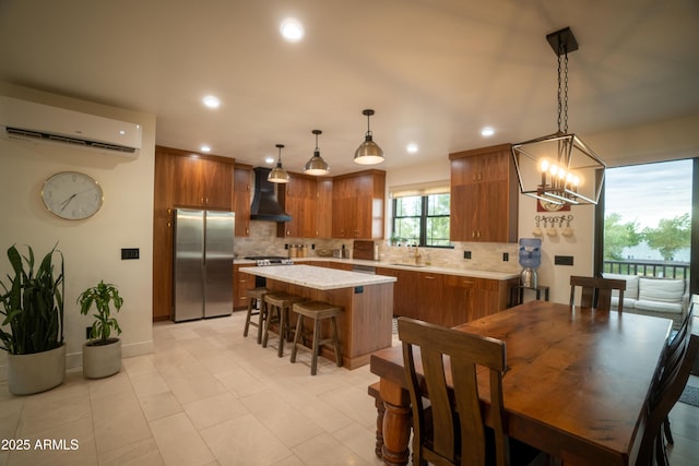 kitchen featuring a kitchen island, freestanding refrigerator, a sink, wall chimney exhaust hood, and brown cabinets