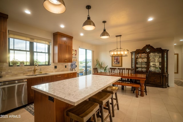 kitchen with dishwasher, a breakfast bar area, decorative backsplash, brown cabinetry, and a sink