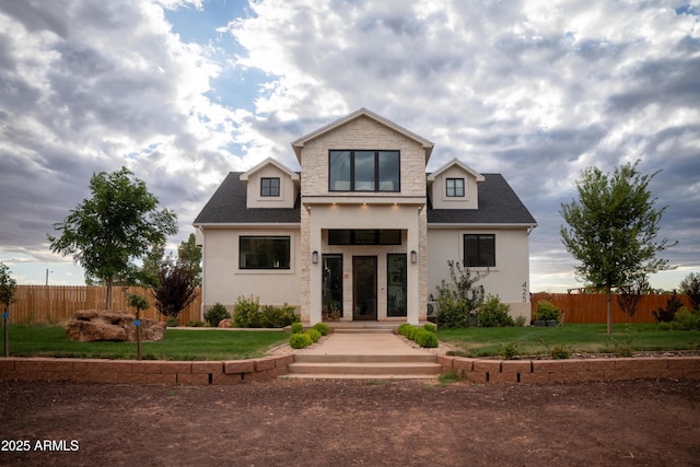 view of front facade featuring a front yard, fence, roof with shingles, and stucco siding