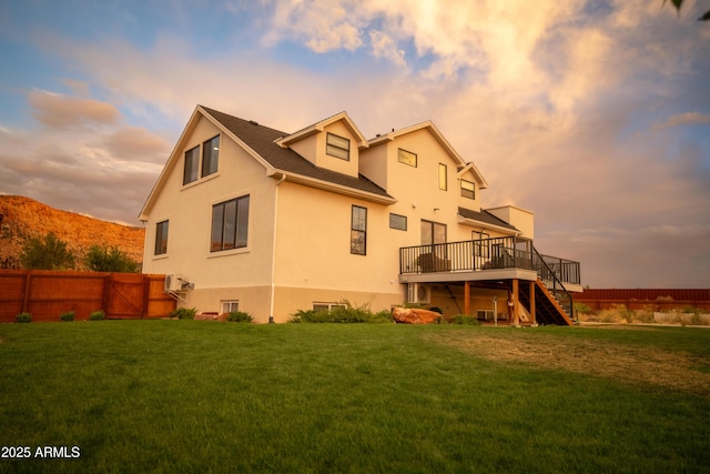 back of house at dusk with stairway, fence, stucco siding, a deck, and a lawn