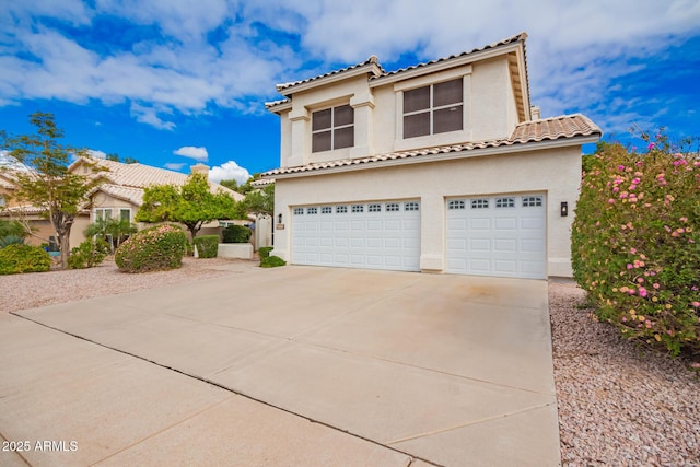 mediterranean / spanish house with a tile roof, an attached garage, concrete driveway, and stucco siding